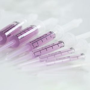 Close-up of several non-sterile plastic syringes filled with light purple liquid, arranged diagonally on a white surface, each fitted with BrandTech PD-Tip II Precision Dispenser Tips, Assorted Sizes (140 count).
