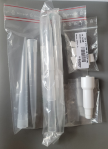 A plastic ziplock bag contains the Macroman Pipette Controller Adapter Kit for D5000 and D10 Tips (Gilson), a syringe filter, and a small labeled bag with folded filter papers on a gray surface.