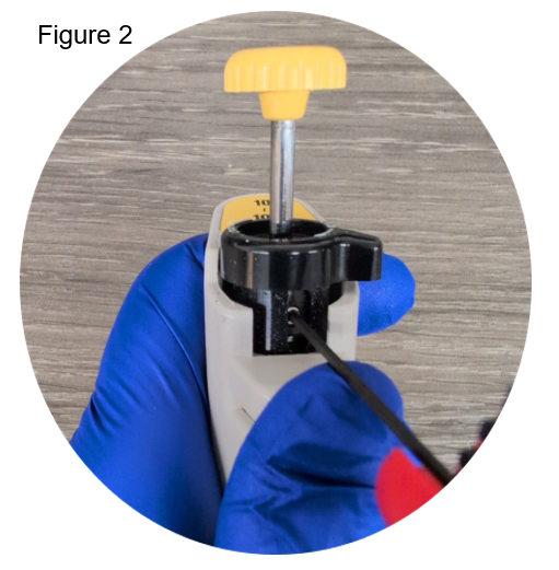 A gloved hand performs a Nichiryo adjustment on a laboratory pipette using a tool inserted into its side, with a yellow knob visible at the top.