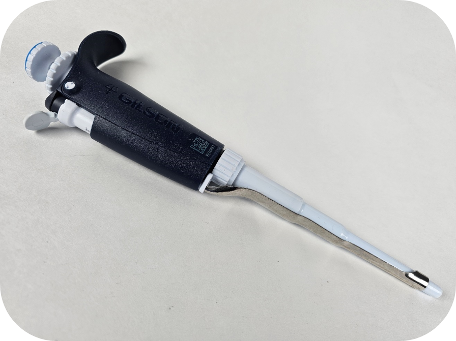 A black and white adjustable pipetman L micropipette is laying on a light, rounded-corner surface.