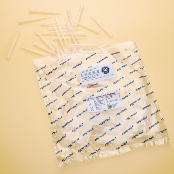 EP 0030080114 A sealed Eppendorf bag labeled “epTIPS BioBased Standard Bulk, 0.25-2.5mL, Red, 500 Tips” contains clear pipette tips, with several tips scattered above it on a light yellow surface.