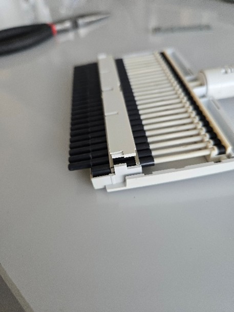 A close-up view of a disassembled pipette lying on a gray surface with pliers in the background.