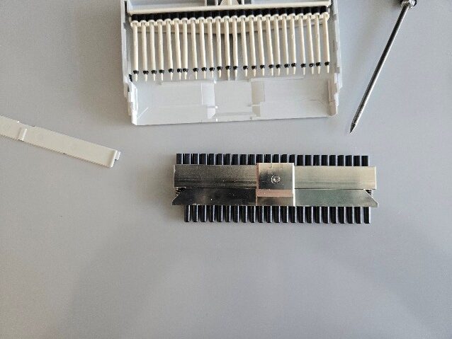 Eppendorf Research Plus Nose cone assembly with metal plate attached, lies next to a disassembled white plastic casing and a screwdriver on a light surface.