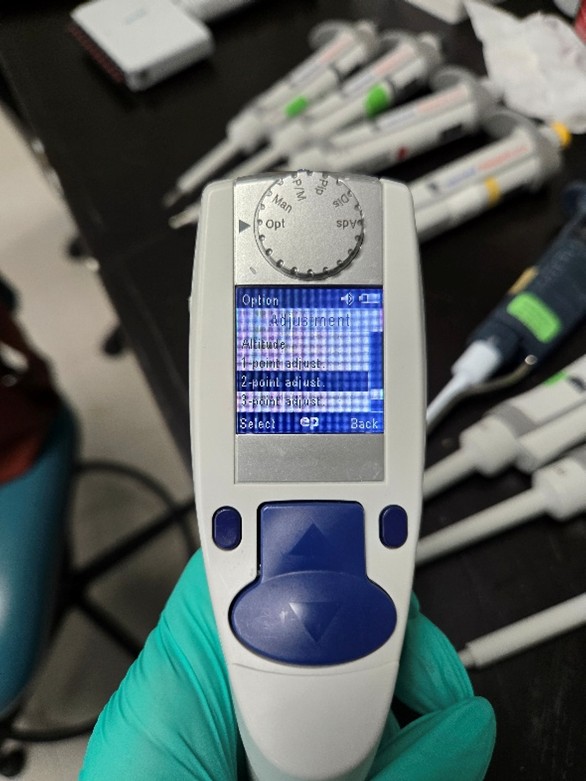 A gloved hand holds the pipette displaying settings on a digital screen, while adjustment instructions are referenced, with additional pipettes and lab equipment visible on a black surface in the background.