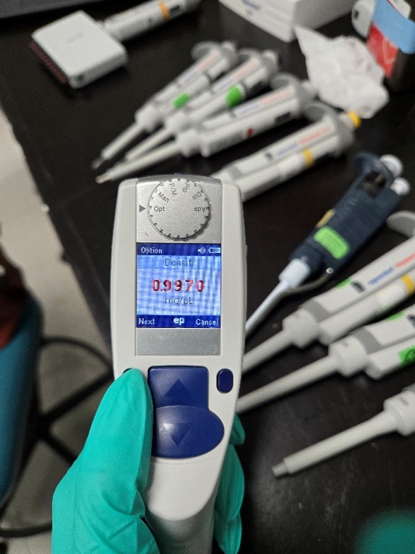 A gloved hand holds an Eppendorf Xplorer electronic pipette showing a display reading “0.9970 mL,” with several manual pipettes lying on a black laboratory bench in the background, hinting at precise Eppendorf Xplorer adjustment.