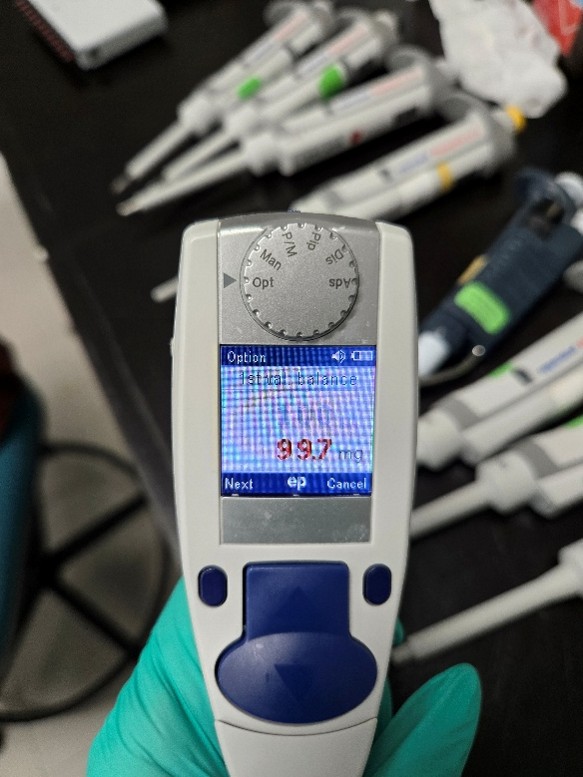A gloved hand holds the pipette displaying 99.7 on its digital screen, with other pipettes and lab equipment visible on the table in the background, ready for precise experiments and easy adjustment instructions.