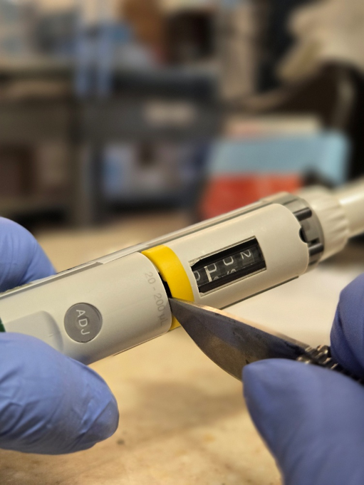 A gloved hand uses a knife to remove the display window with the counter assembly and adjustment button visible—similar care and precision required in pipette calibration or Eppendorf Research Plus calibration.